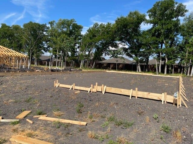 Form boards set along one edge of a graded pad, with framing under way on the next lot.