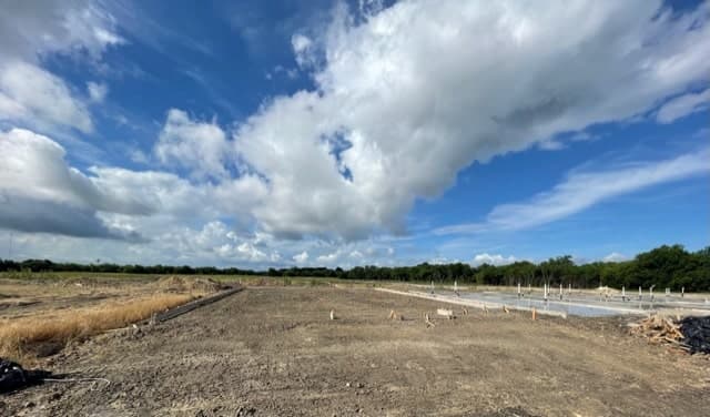 Graded building pad on a new subdivision lot, with slabs under construction in the distance.