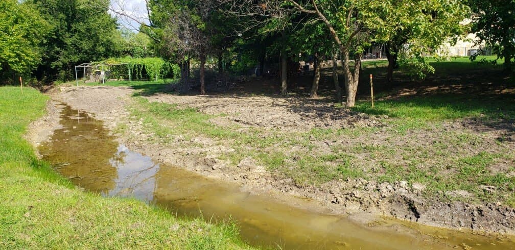 Drainage channel running through a treed residential lot, documented for a topographic survey.
